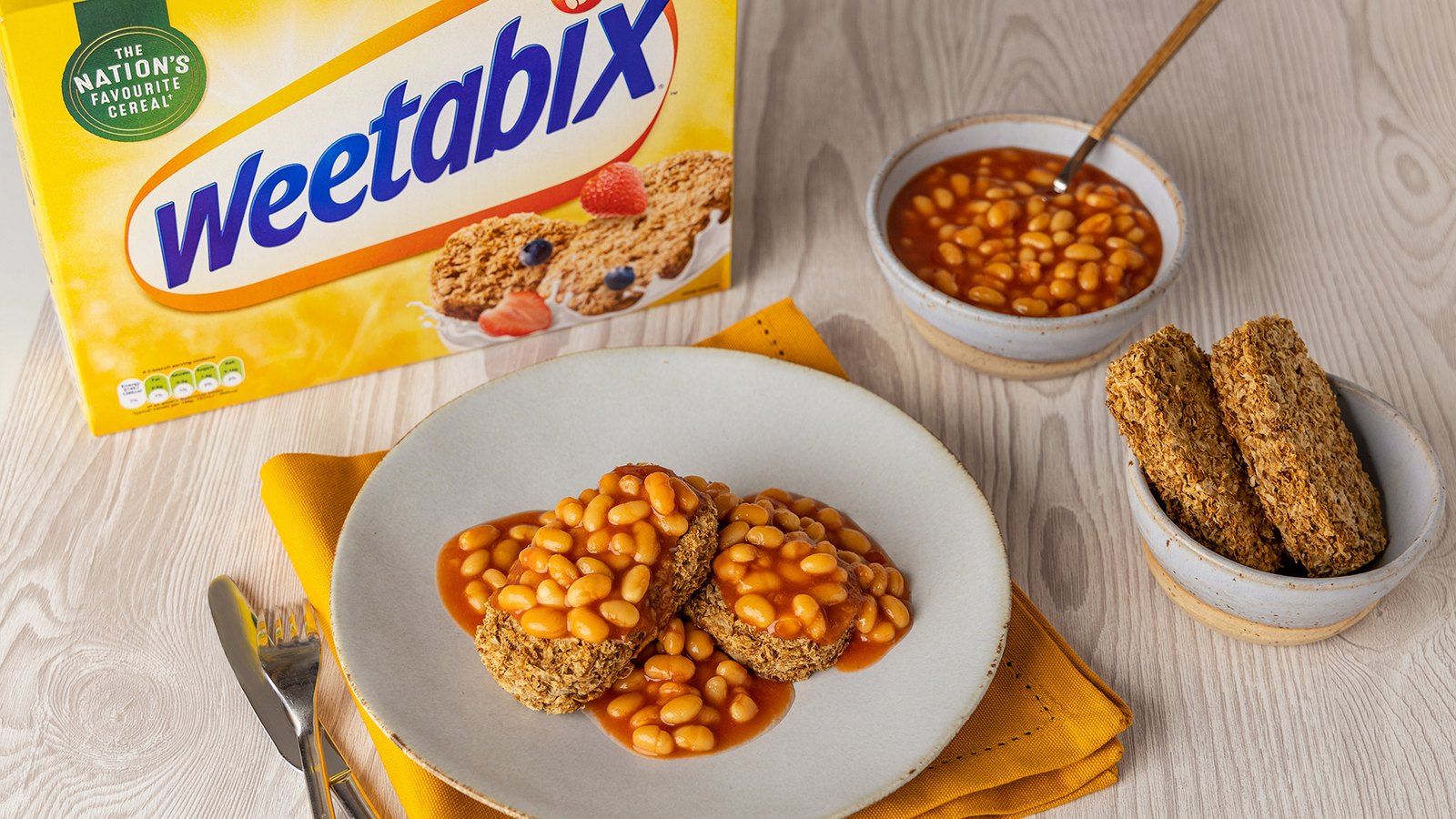 Weetabix biscuits topped with baked beans on a plate next to a Weetabix box