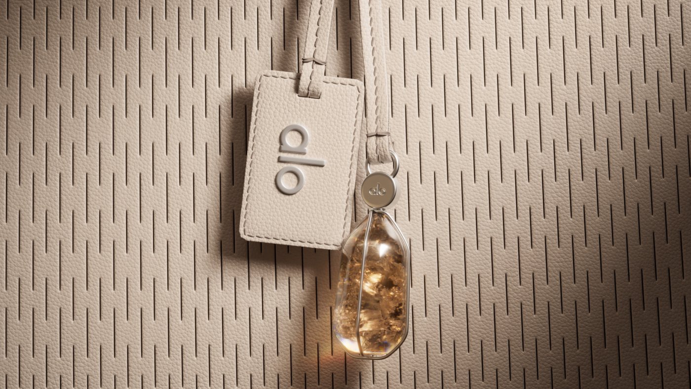 A 3D render of a cream leather tag embossed with the alo logo and a crystal charm hanging against a perforated leather surface