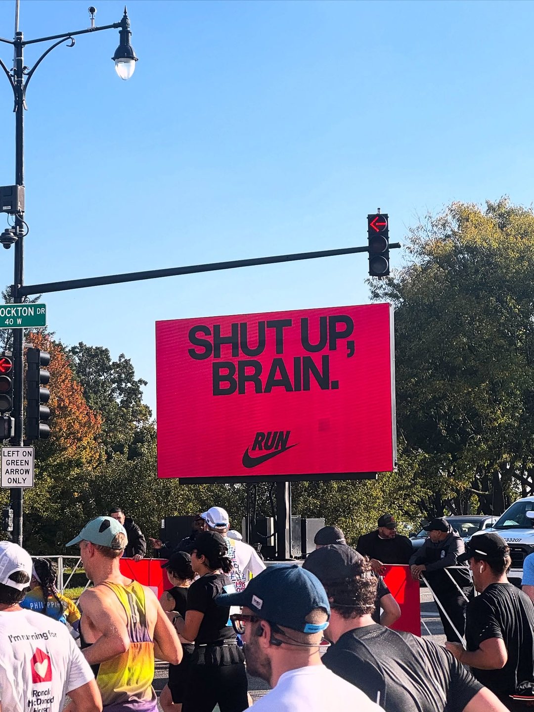A red Nike digital board reading Shut up, brain above marathon runners on a Chicago street, signed Run with the swoosh