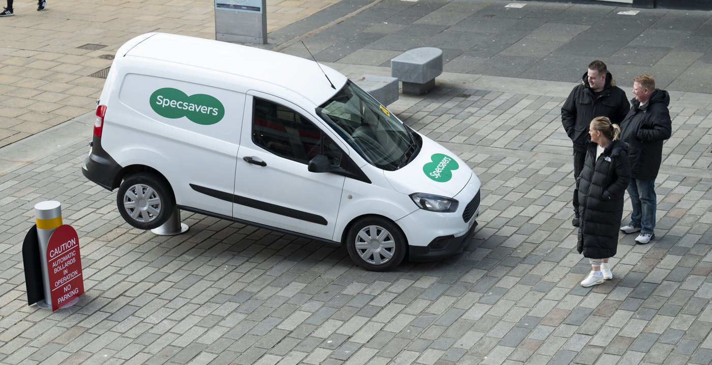 A Specsavers van stuck on top of a rising bollard in a pedestrian street, with a warning sign about automatic bollards beside it