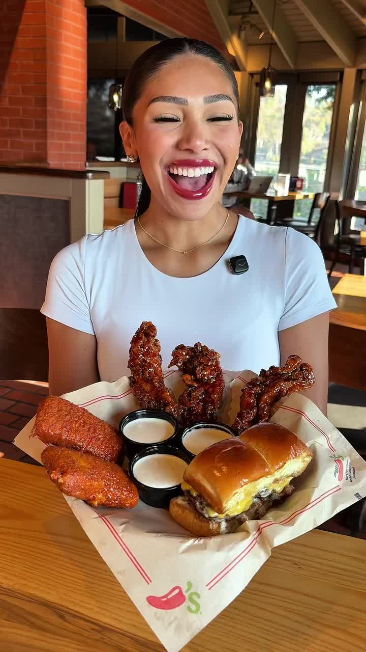 A creator smiling behind a Chili's Triple Dipper platter with mozzarella sticks and sliders in a TikTok video