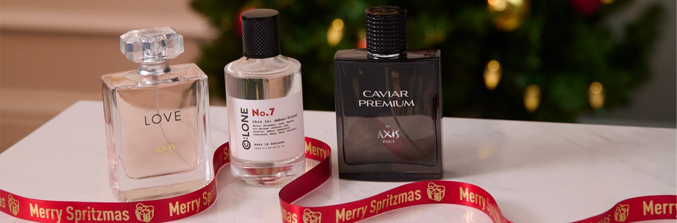 Three fragrance bottles on a table with red Merry Spritzmas ribbon and a Christmas tree behind